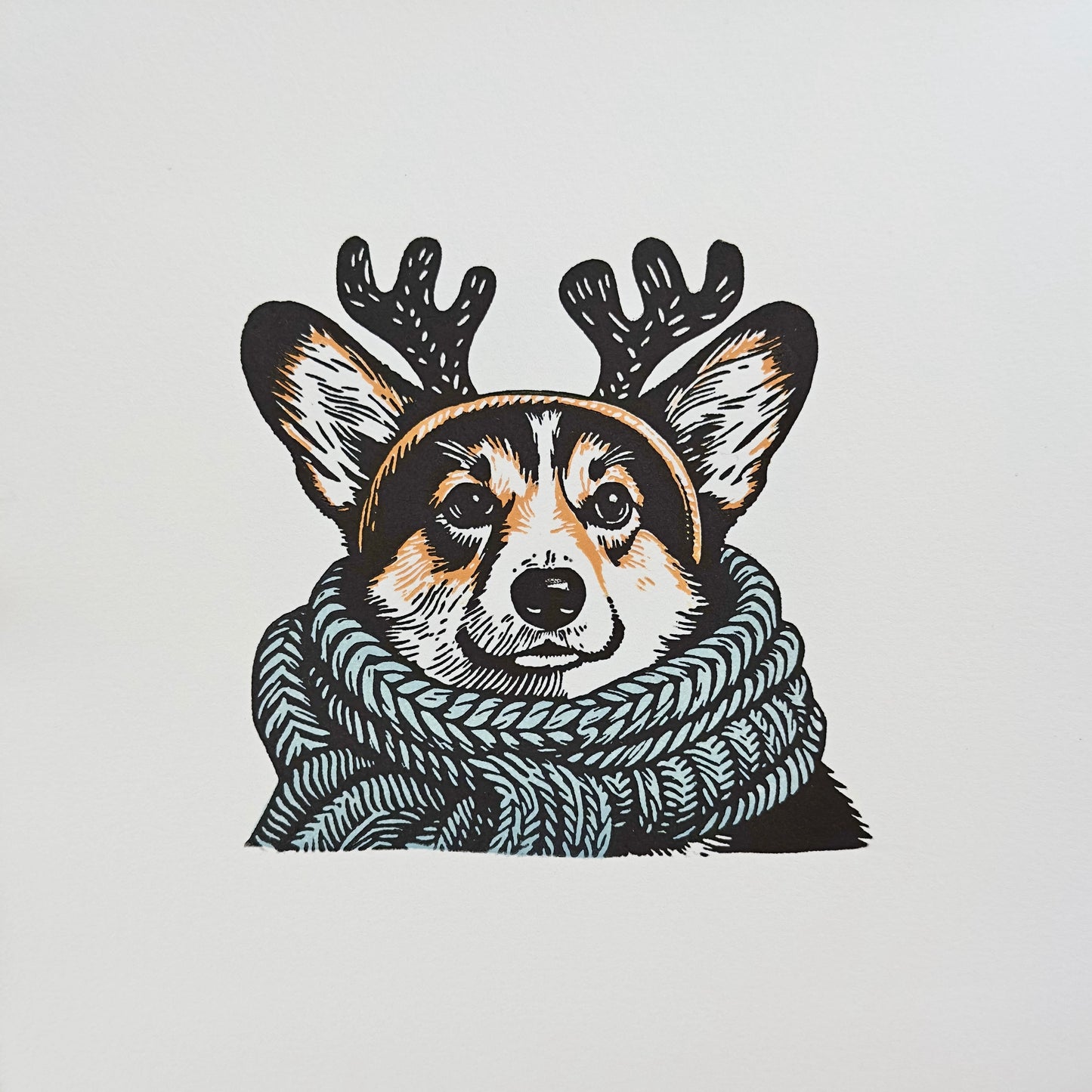 Multi-colour linocut print of a tricolour Pembroke corgi, predominantly black, white, and tan, adorned with an oversized, powder blue knitted scarf wrapped around its neck. The corgi is also wearing a headband with cute antlers, giving it a festive look. The print has a plain white background, which highlights the detailed and colourful depiction of the corgi. Perfect gift for a corgi dog lover and art lovers.