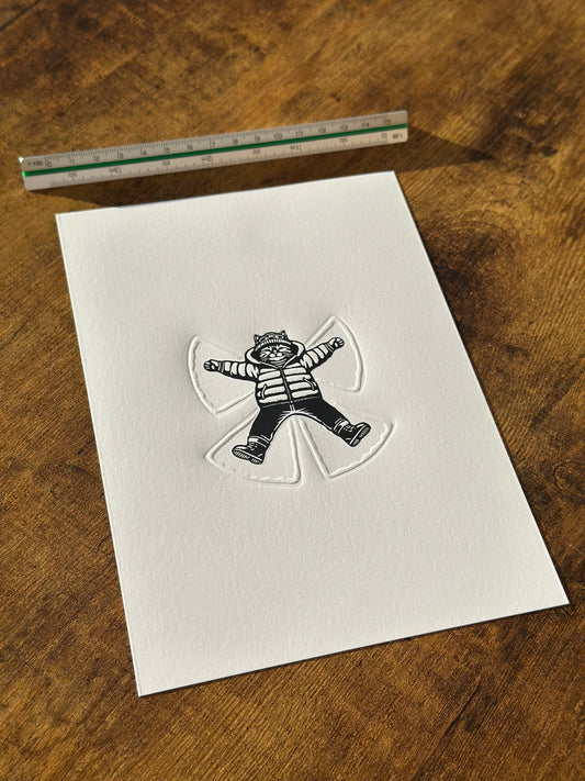 A cat making a snow angel - a perfect linocut print with embossed elements