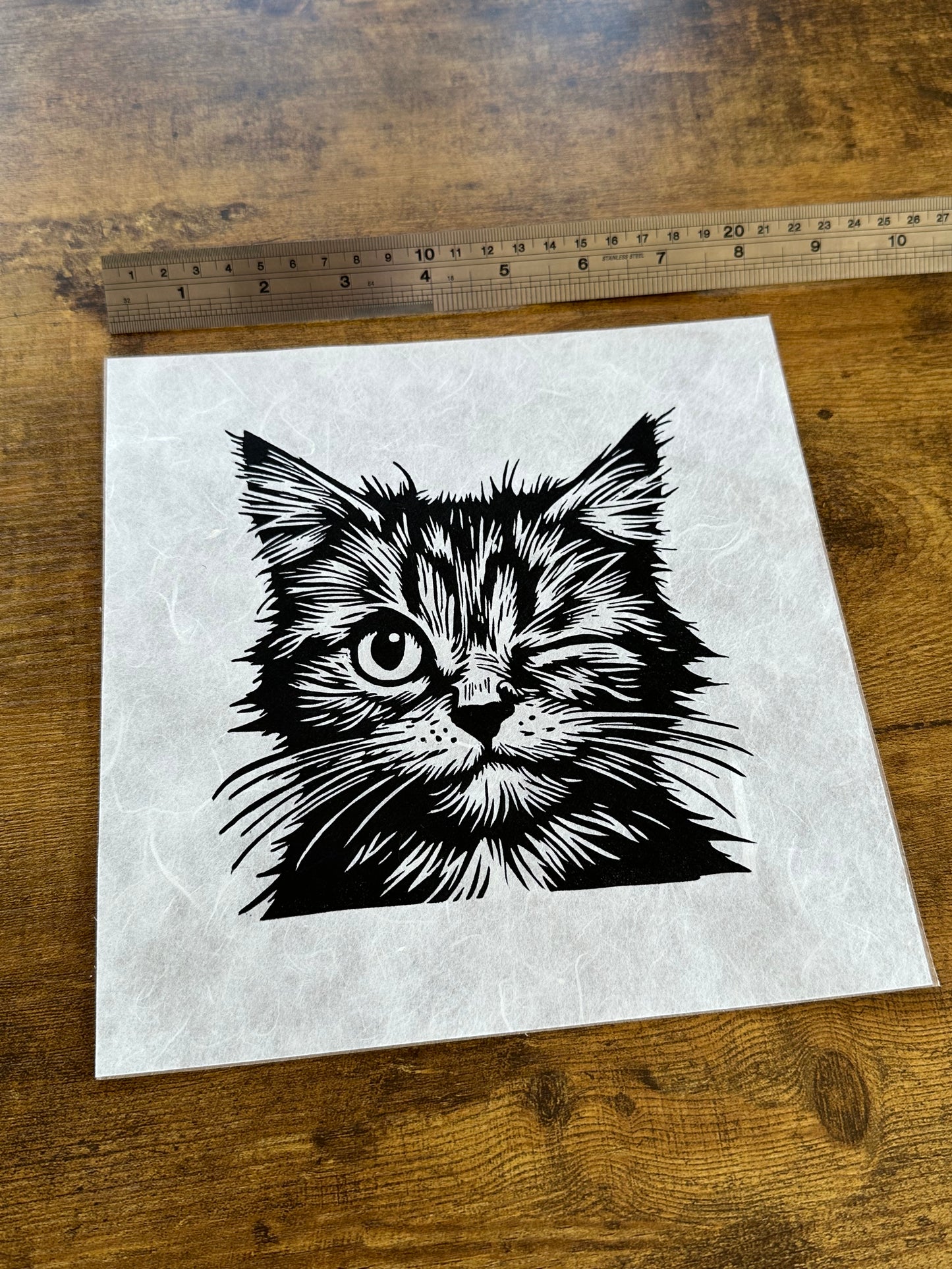 Linocut print of a playful cat winking, with bold, textured lines and a cheeky expression.