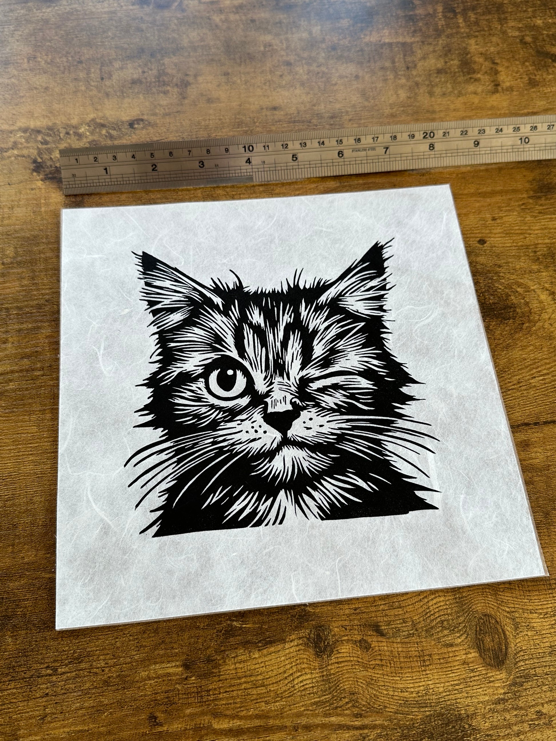 Linocut print of a playful cat winking, with bold, textured lines and a cheeky expression.