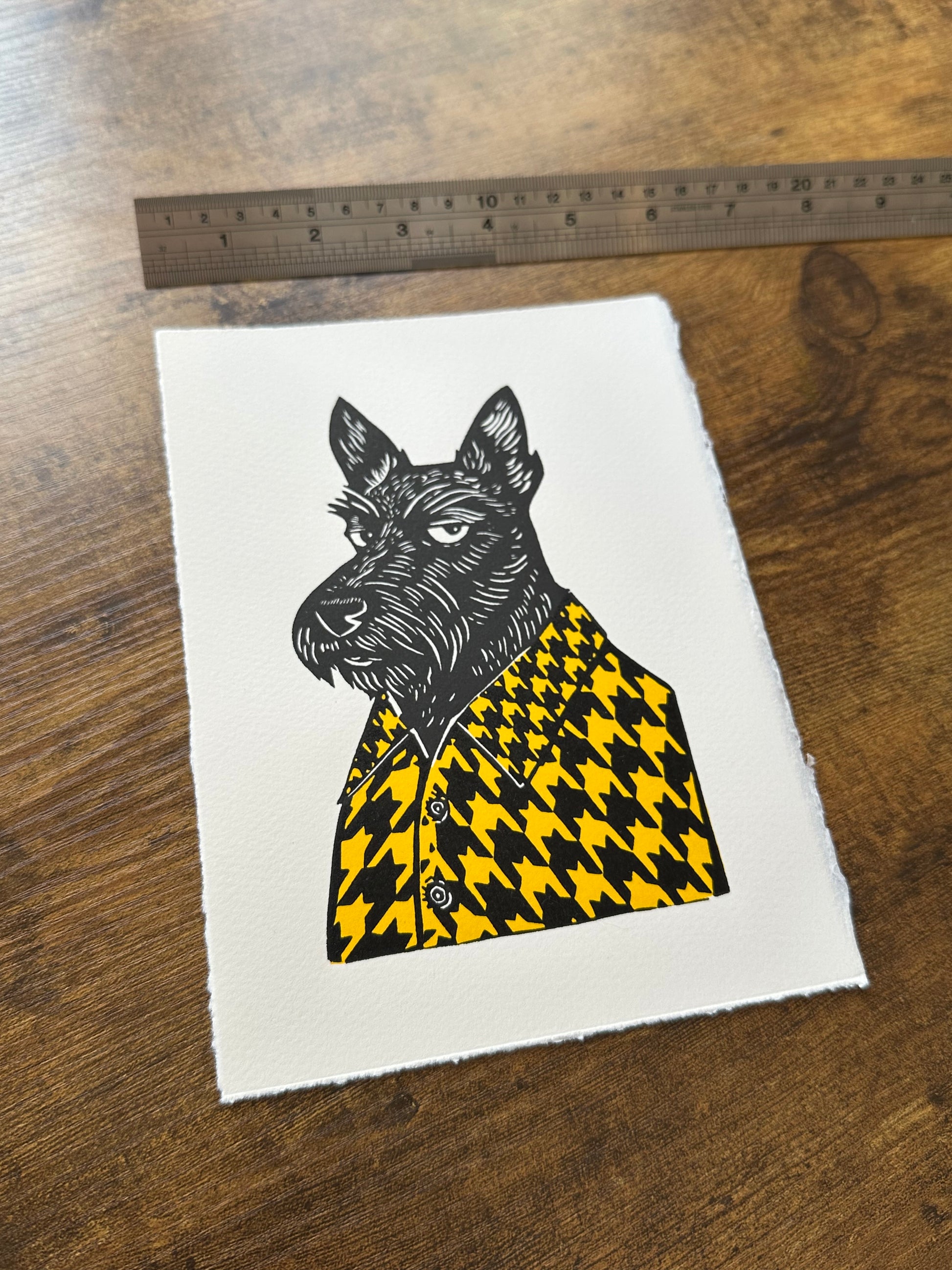 Black and white linocut print of a Scottish terrier wearing a houndstooth-patterned coat in yellow, showcasing bold textures and classic design.