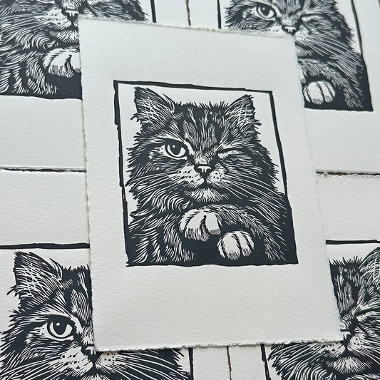 Linocut print of a cat with paws crossed and winking 