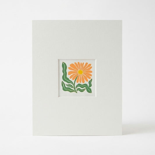 A linocut print featuring a stylised orange flower with green leaves in the centre, photographed against a clean white background.