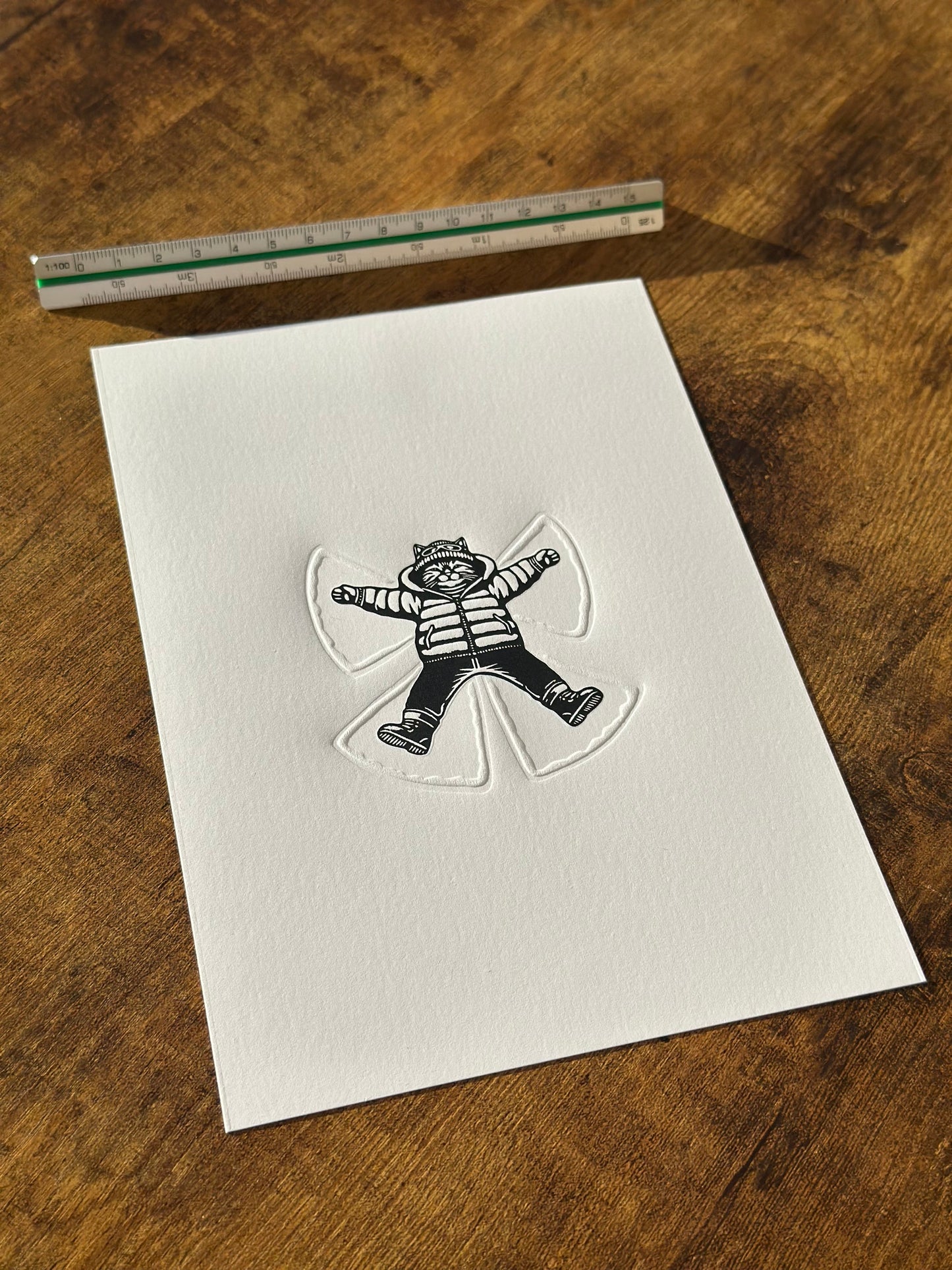 A cat making a snow angel - a perfect linocut print with embossed elements