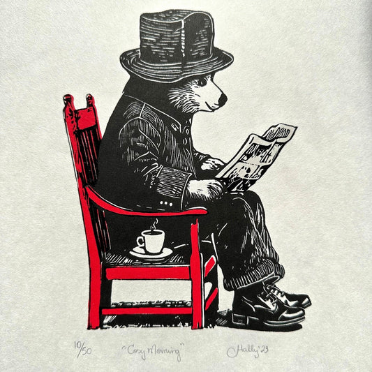 An anthropomorphic bear sits reading a newspaper with a cup of tea beside him. This linocut print features intricate details and is ideal for bear lovers.